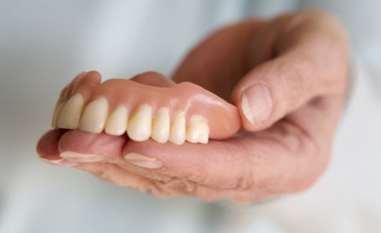 Hand holding full dentures for upper arch